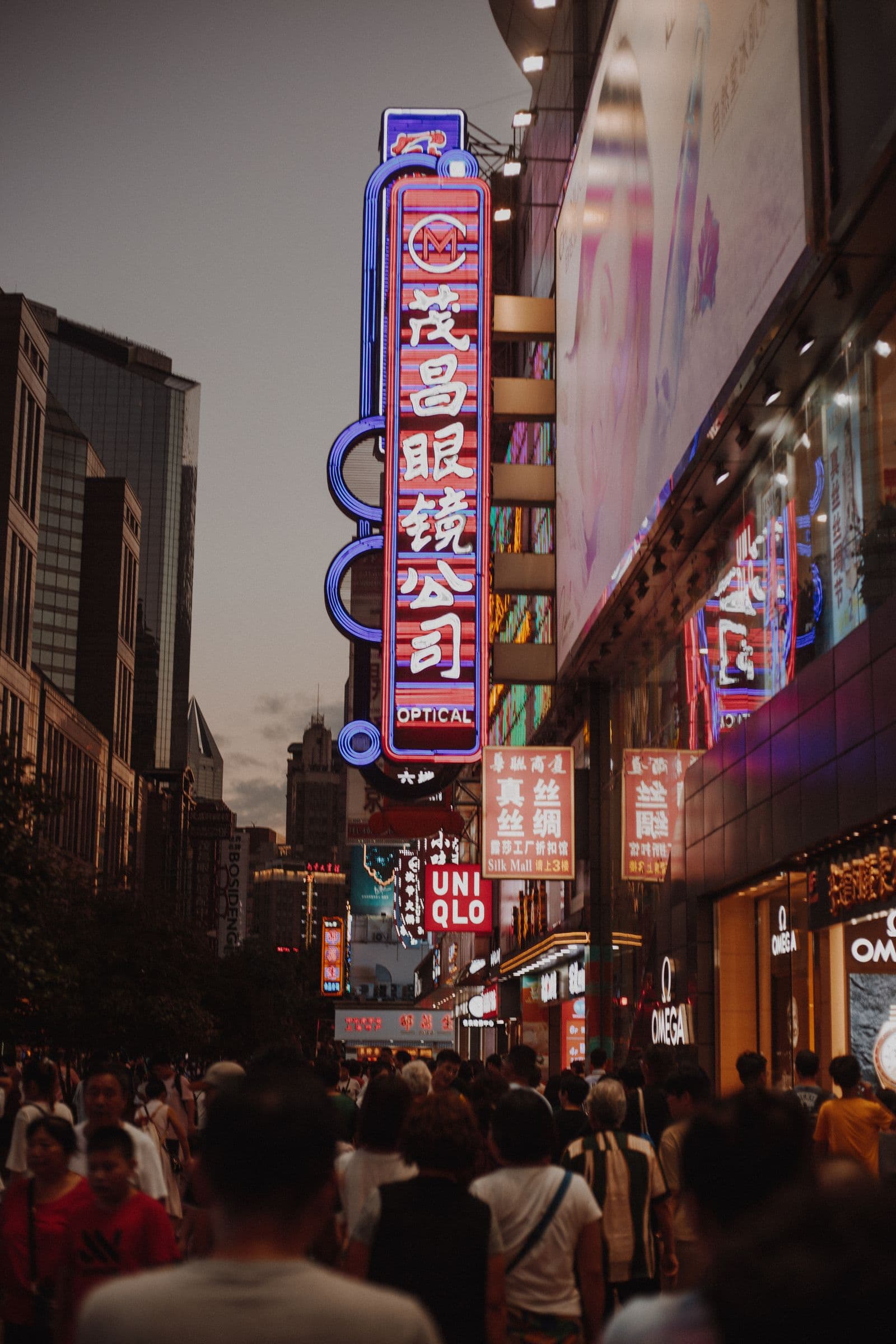 People exploring Nanjing Road in Shanghai beneath illuminated signs at dusk