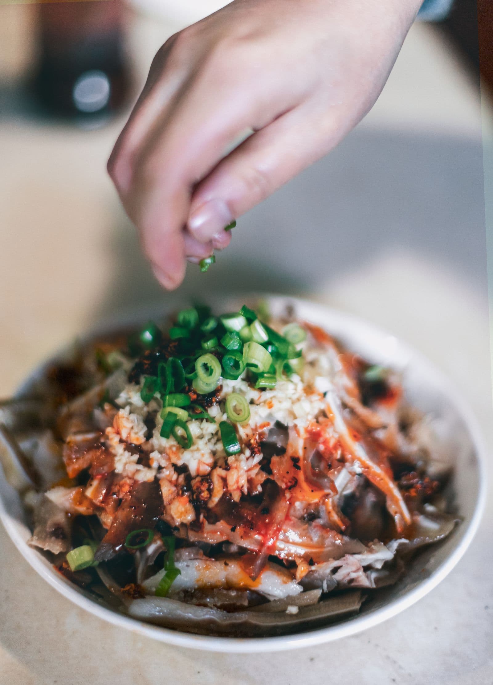 A hand adding fresh green onions to a Sichuan dish in Liangshan, China